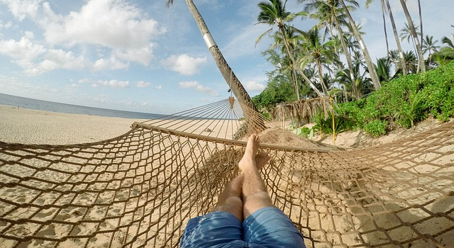 Ein Mitarbeiter einer Firma macht an einem Strand mit Palmen Urlaub in der Hängematte Ein Mitarbeiter einer Firma macht an einem Strand mit Palmen Urlaub in der Hängematte